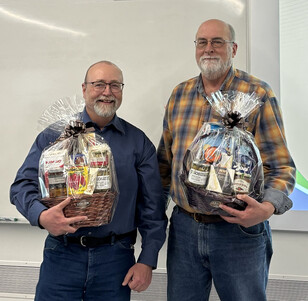 Two men stand by a side holding gift baskets.
