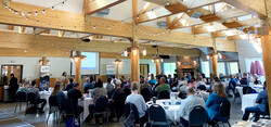 People sitting at tables talking in spacious room with wood beams overhead.