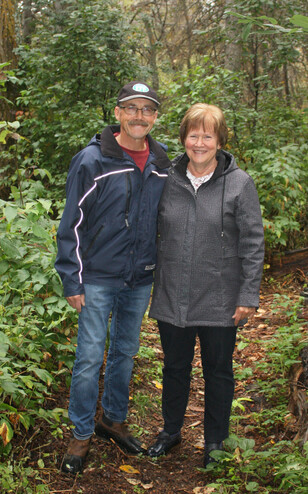 A couple pose on a path in the forest.