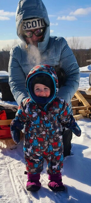 A woman and her daughter stand in the snow wearing snowsuits on a sunny day.