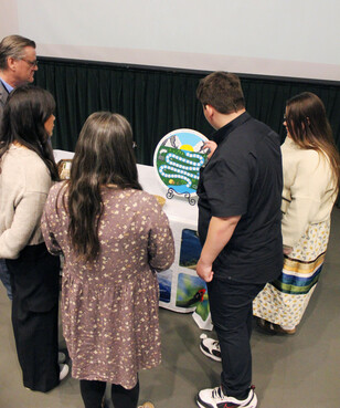 People stand around a boardgame as one youth explains the game.