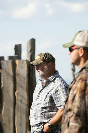 Man listening with another man by a fence.