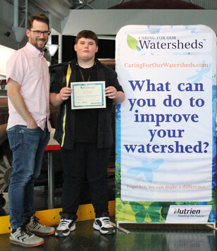 Man and teen stand next to a poster about caring for watersheds.