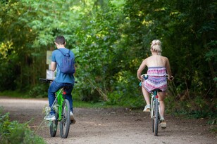 Young man and woman bike along a treed path.